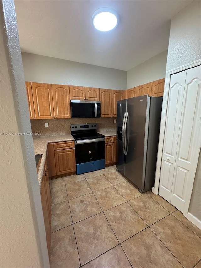 kitchen with stainless steel microwave, light countertops, refrigerator with ice dispenser, range with electric stovetop, and light tile patterned floors