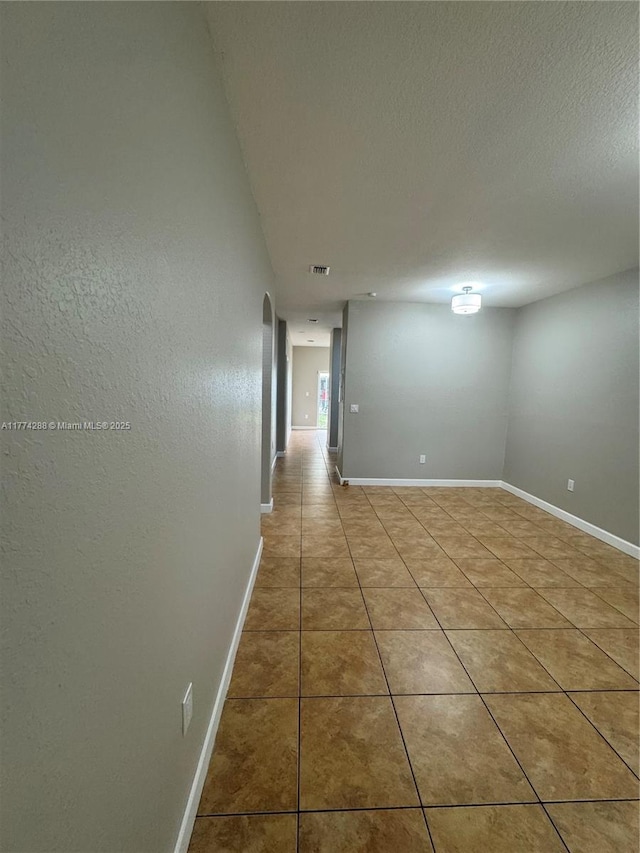 empty room with baseboards, arched walkways, a textured ceiling, and light tile patterned floors