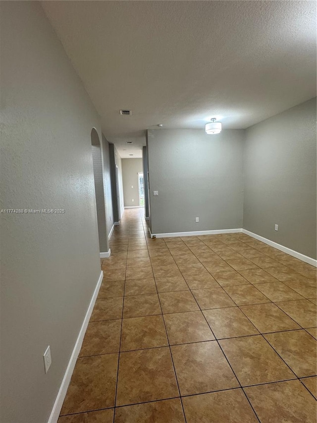 empty room with baseboards, a textured ceiling, and light tile patterned floors