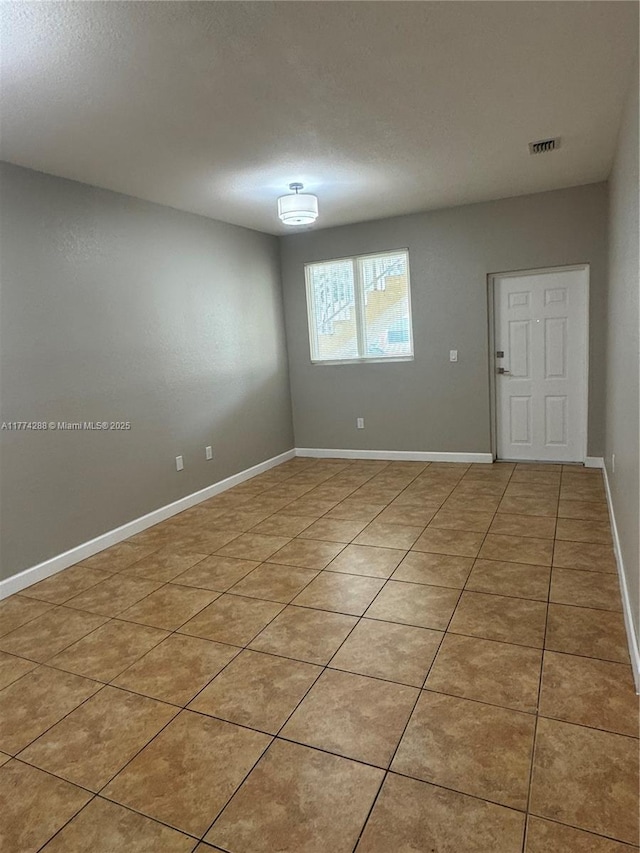 empty room with light tile patterned flooring, a textured ceiling, baseboards, and visible vents