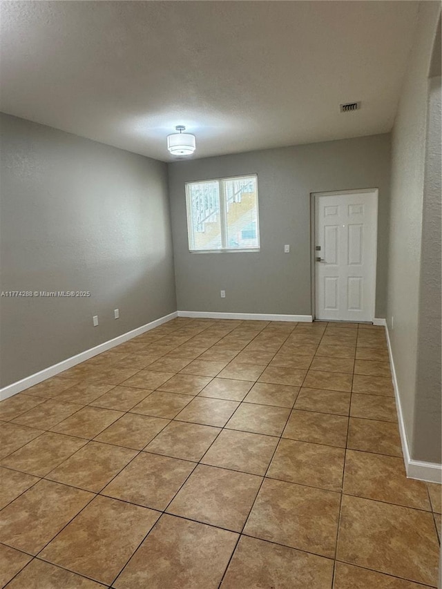 empty room with light tile patterned flooring, visible vents, and baseboards