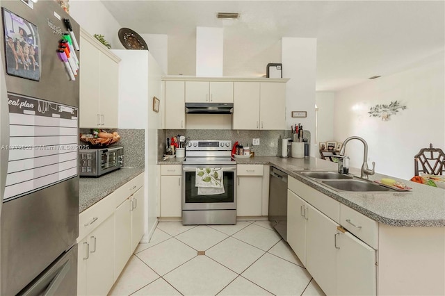 kitchen featuring a peninsula, under cabinet range hood, a sink, stainless steel appliances, and backsplash