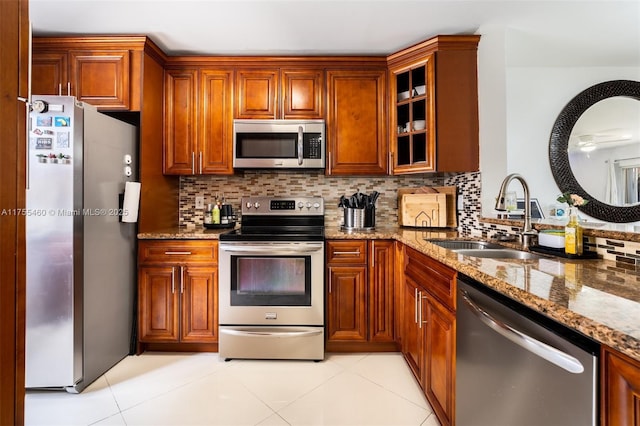 kitchen featuring glass insert cabinets, stone countertops, a sink, stainless steel appliances, and decorative backsplash