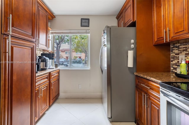 kitchen featuring light tile patterned floors, baseboards, appliances with stainless steel finishes, decorative backsplash, and stone countertops