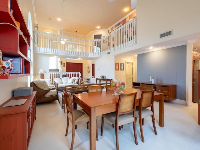 dining room featuring a towering ceiling, visible vents, a ceiling fan, and ornamental molding