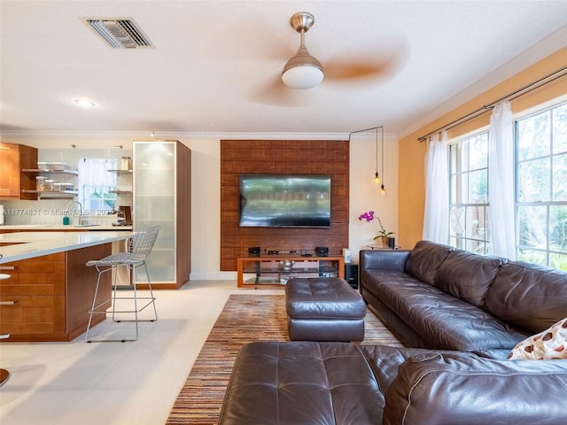 living area with visible vents, ornamental molding, and a ceiling fan