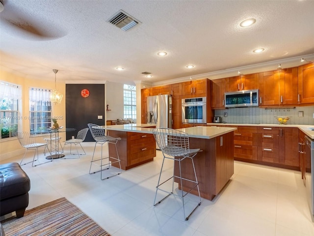 kitchen with a kitchen bar, a center island, brown cabinets, stainless steel appliances, and visible vents