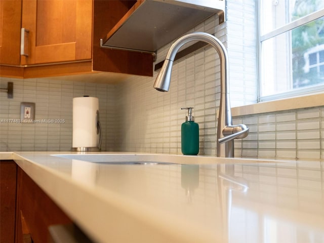 details featuring under cabinet range hood, backsplash, and brown cabinetry