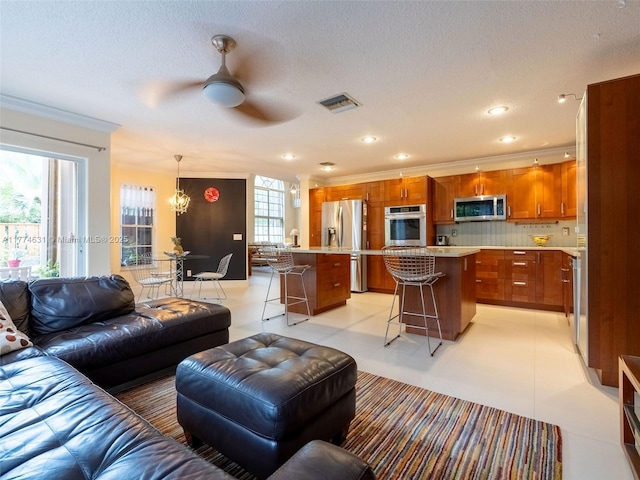 living area featuring crown molding, a wealth of natural light, visible vents, and ceiling fan with notable chandelier