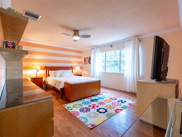 bedroom with a textured ceiling, visible vents, crown molding, and wood finished floors