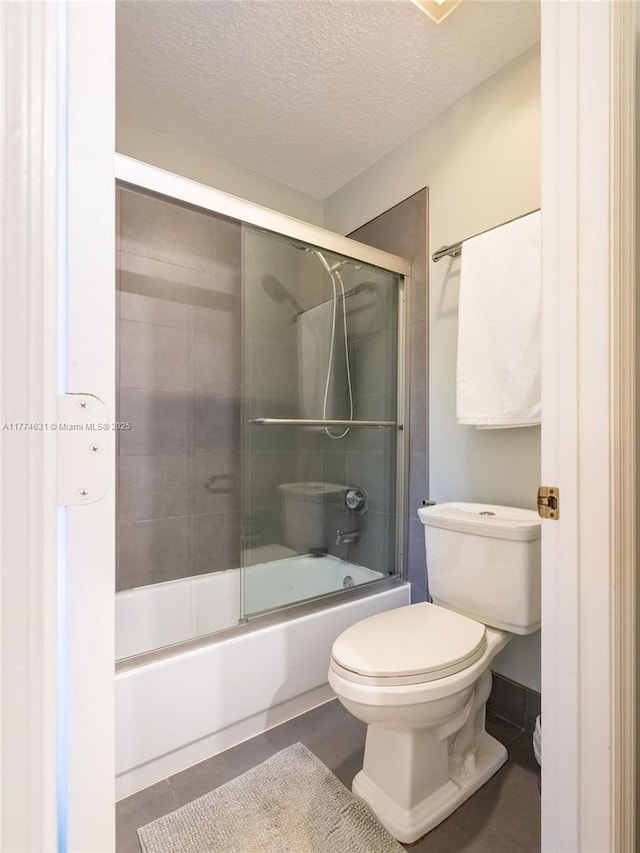 full bathroom featuring a textured ceiling, toilet, tile patterned flooring, and bath / shower combo with glass door