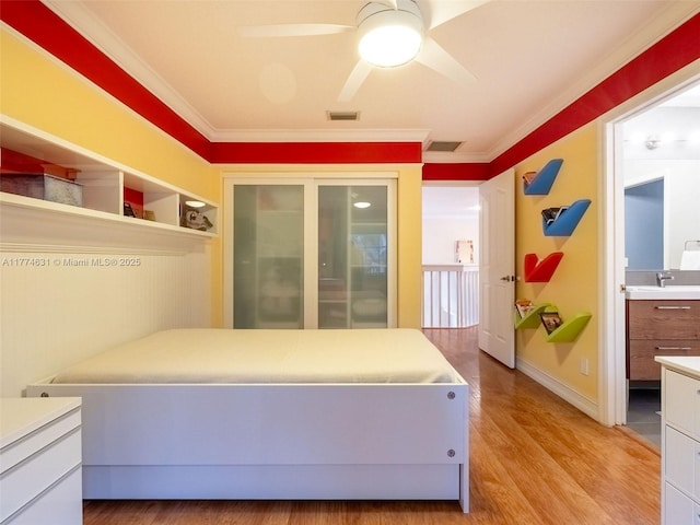 bedroom featuring a sink, visible vents, light wood-style floors, and ornamental molding