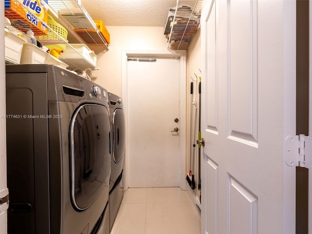 clothes washing area with washing machine and dryer, a textured ceiling, laundry area, and light tile patterned floors