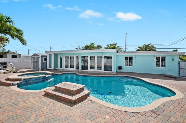 view of swimming pool featuring a pool with connected hot tub, a patio area, a storage unit, fence, and french doors
