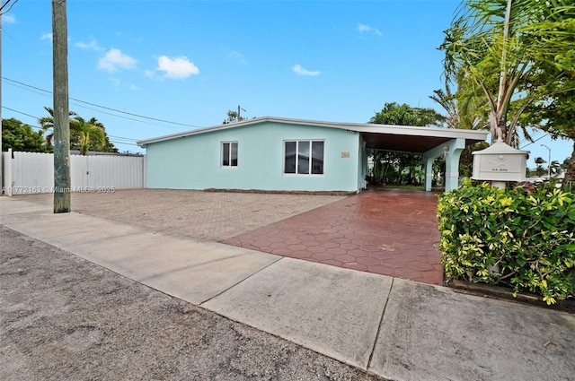 view of front of property featuring a carport, fence, driveway, and stucco siding