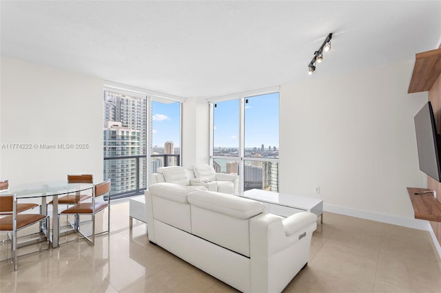 living room featuring baseboards, rail lighting, light tile patterned floors, and a wall of windows