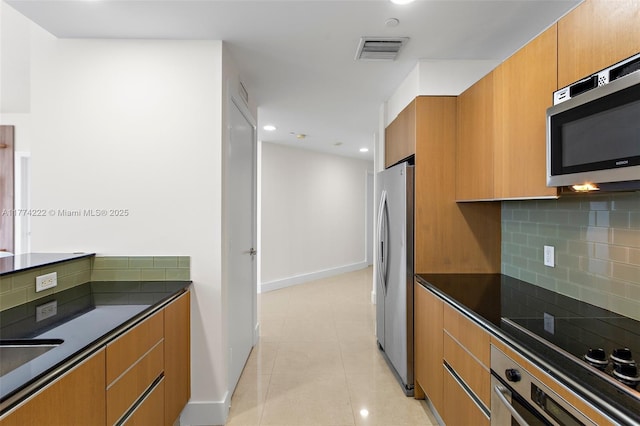 kitchen with decorative backsplash, visible vents, brown cabinets, dark countertops, and appliances with stainless steel finishes