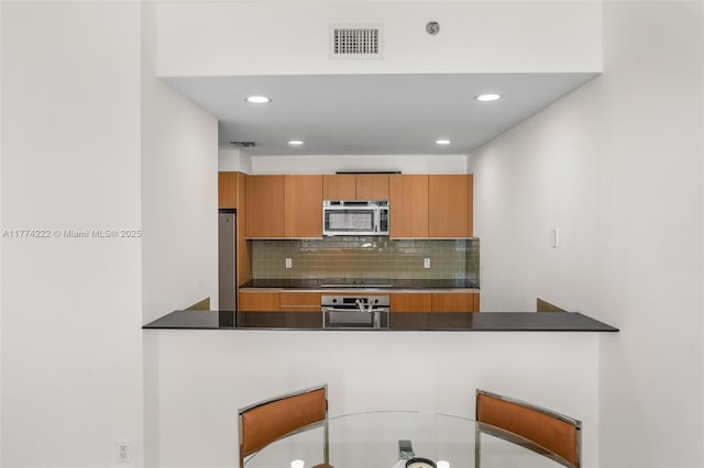 kitchen with visible vents, stainless steel appliances, dark countertops, and a peninsula