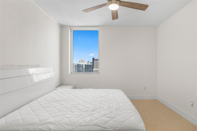 bedroom featuring a city view, baseboards, light colored carpet, and ceiling fan
