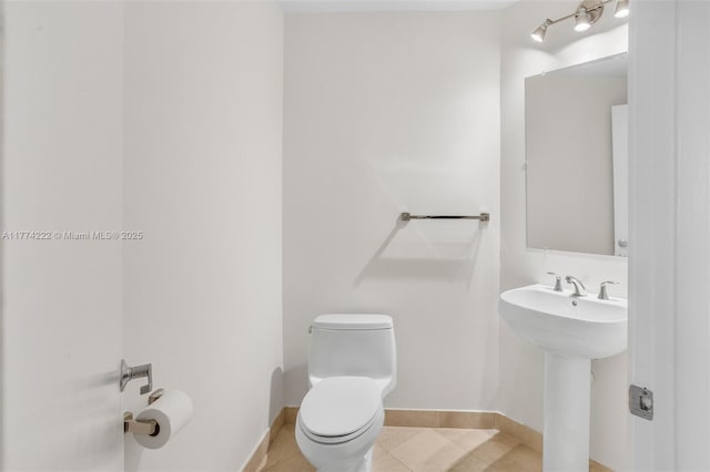bathroom featuring baseboards, toilet, tile patterned floors, and a sink