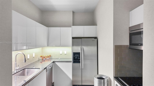 kitchen featuring white cabinets, a sink, stainless steel appliances, and backsplash