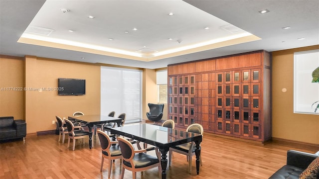 dining room featuring baseboards, light wood finished floors, and a raised ceiling