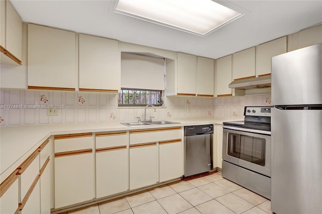 kitchen with a sink, cream cabinetry, under cabinet range hood, light countertops, and appliances with stainless steel finishes