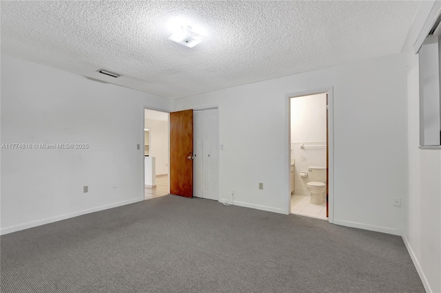 unfurnished bedroom featuring connected bathroom, a textured ceiling, visible vents, and carpet floors