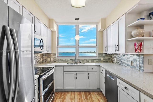 kitchen with light wood finished floors, a sink, tasteful backsplash, open shelves, and appliances with stainless steel finishes
