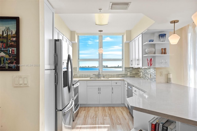kitchen featuring light wood finished floors, stainless steel appliances, a sink, visible vents, and backsplash