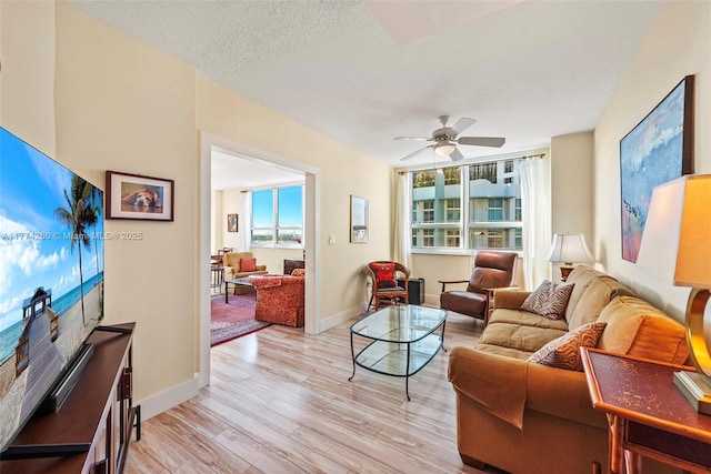 living area with baseboards, a textured ceiling, light wood-style floors, and ceiling fan