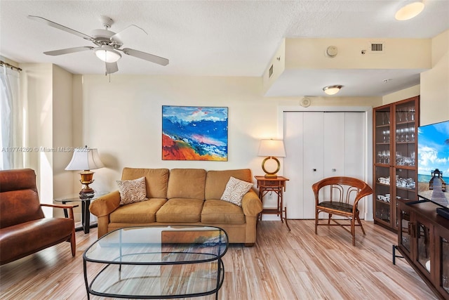 living area with light wood-style flooring, a textured ceiling, and a ceiling fan