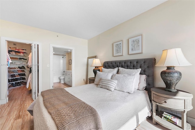 bedroom featuring a spacious closet, ensuite bath, light wood-style floors, and a closet