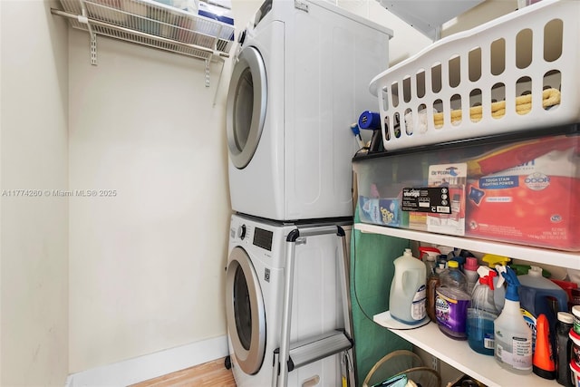 clothes washing area with wood finished floors, stacked washer and dryer, baseboards, and laundry area