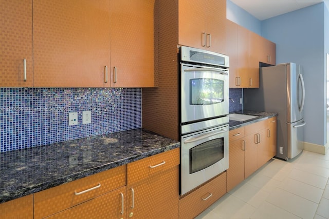 kitchen with stainless steel appliances, decorative backsplash, dark stone countertops, and light tile patterned floors