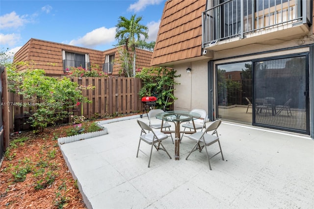 view of patio featuring outdoor dining space, fence, and a balcony