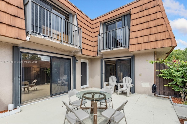 back of property with a patio area, mansard roof, outdoor dining area, and stucco siding