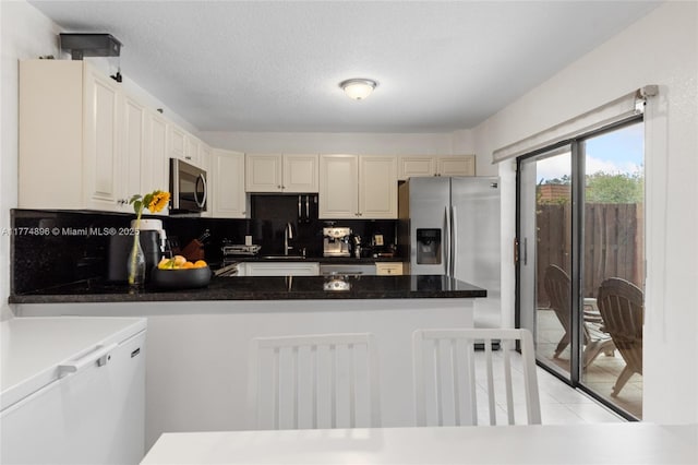 kitchen with light tile patterned floors, a peninsula, appliances with stainless steel finishes, a sink, and decorative backsplash