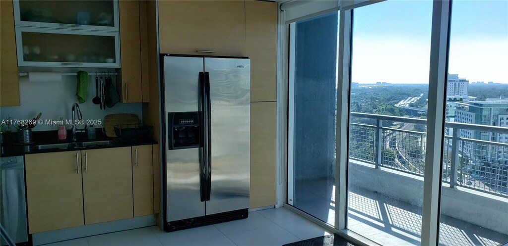 kitchen with stainless steel refrigerator with ice dispenser, a sink, dark countertops, a city view, and glass insert cabinets