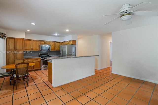 kitchen with brown cabinets, stainless steel appliances, a ceiling fan, decorative backsplash, and light tile patterned floors