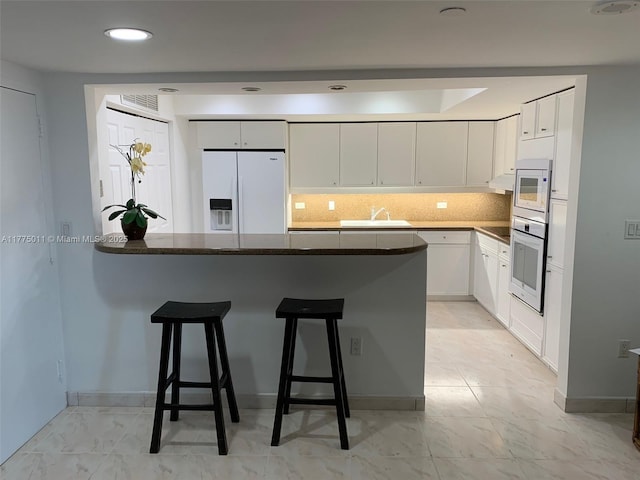 kitchen featuring a sink, a breakfast bar, white appliances, a peninsula, and backsplash
