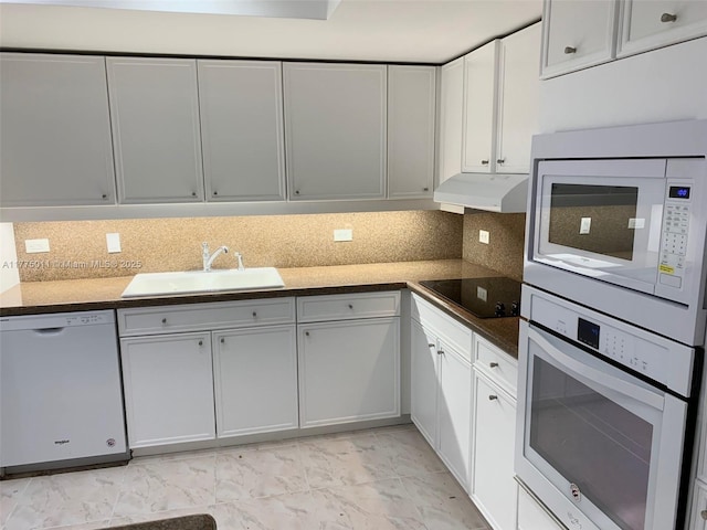 kitchen with a sink, dark countertops, white appliances, under cabinet range hood, and backsplash