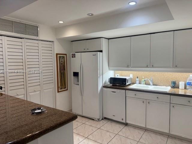 kitchen with white appliances, backsplash, light tile patterned flooring, visible vents, and a sink