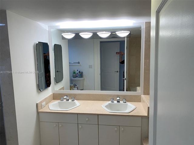bathroom with double vanity, a sink, and toilet