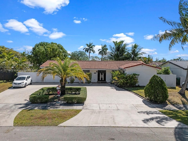 mediterranean / spanish-style house featuring driveway, fence, a tiled roof, and stucco siding