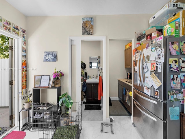 kitchen featuring baseboards, marble finish floor, a sink, and stainless steel fridge
