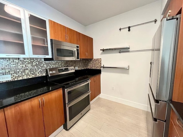 kitchen featuring decorative backsplash, baseboards, brown cabinets, appliances with stainless steel finishes, and glass insert cabinets