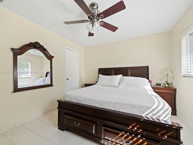 bedroom featuring baseboards, a textured ceiling, ceiling fan, and light tile patterned floors