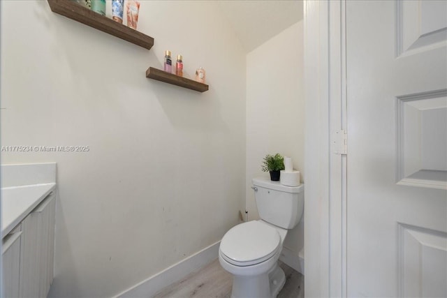 bathroom with baseboards, wood finished floors, toilet, and vanity