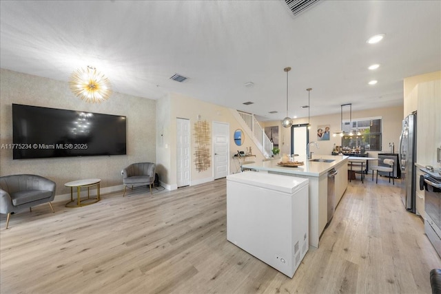kitchen with a sink, stainless steel appliances, light wood-style floors, and a center island with sink